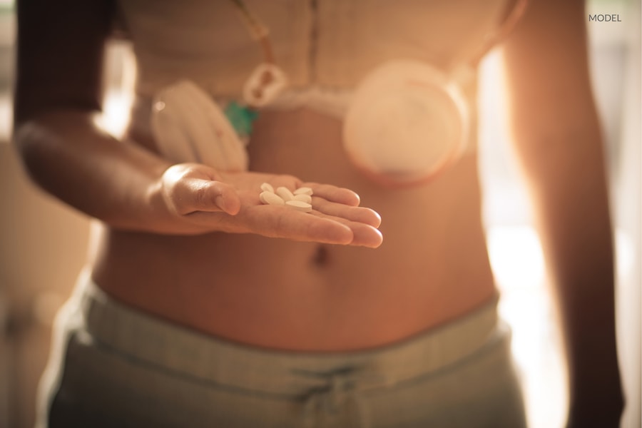 A woman holding pain reliving medication while wearing a compression garment after breast augmentation.